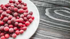 A plate of many frozen cranberries sits on a wooden table.