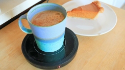 A mug of coffee on an electric mug warmer and a slice of pie in the background.