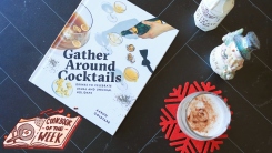 Gather Around Cocktails book on a table with eggnog in a glass.