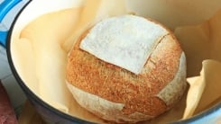 A loaf of bread in a blue dutch oven pot.