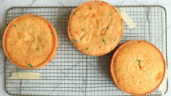 Three Funfetti cake layers on a wire cooling rack.