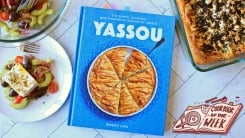The Yassou cookbook on a counter top with a salad and bread.
