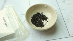Nigella seeds in a small bowl next to a bag labeled "Nigella Seed."