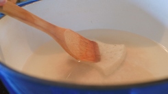 A wooden spoon cleaning with a sponge in a Dutch oven.
