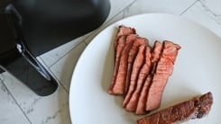 Steak slices on a plate next to an air fryer basket.
