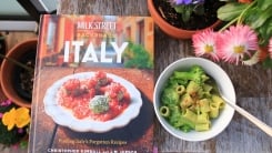 Backroads Italy cookbook on a table with flowers next to a bowl of broccoli pasta.