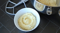 Thick mashed potatoes in a bowl next to a mixing bowl and paddle attachment.