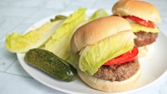 Two hamburgers on a plate with lettuce and pickles.
