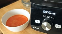 A bowl of tomato soup next to the Vitamix blender base.