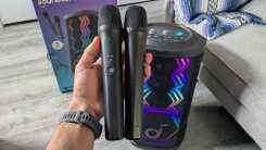 My hand holding the Soundcore Rave 3S microphones in my office with the Soundcore Rave 3S speaker in the back.