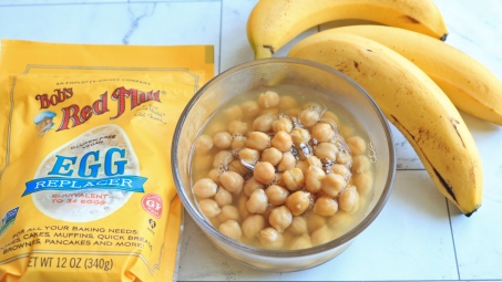 Bob's Red Mill egg replacement next to a bowl of chickpeas in aquafaba and a few bananas.