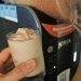 A hand holding a milkshake in front of the Ninja Slushi machine