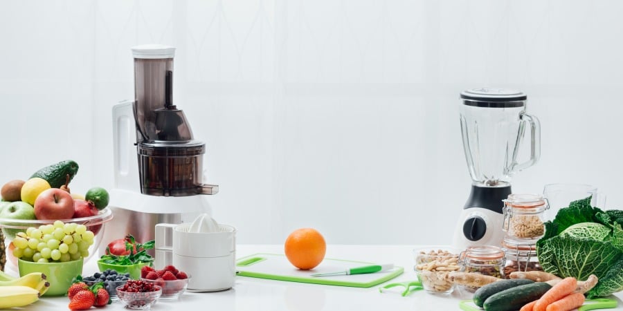 A juicer and a blender on a counter with fruits and veggies