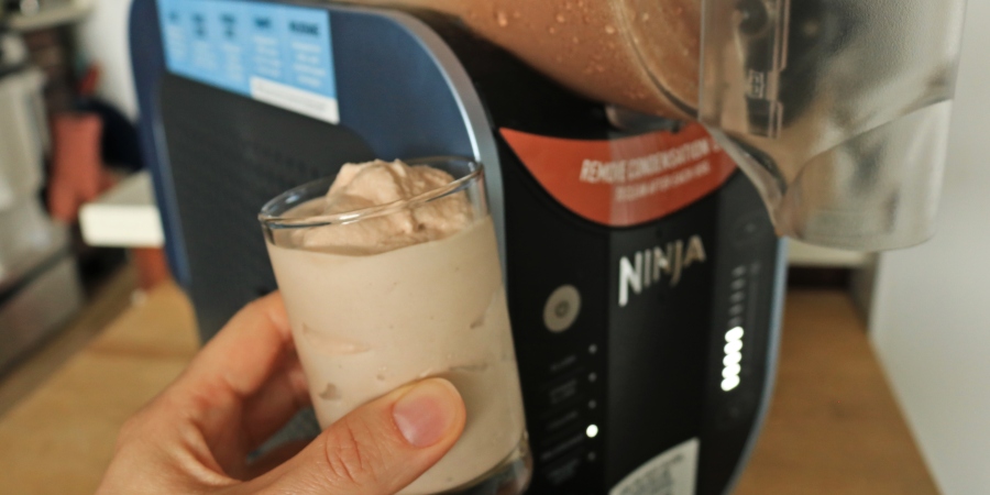 A hand holding a milkshake in front of the Ninja Slushi machine