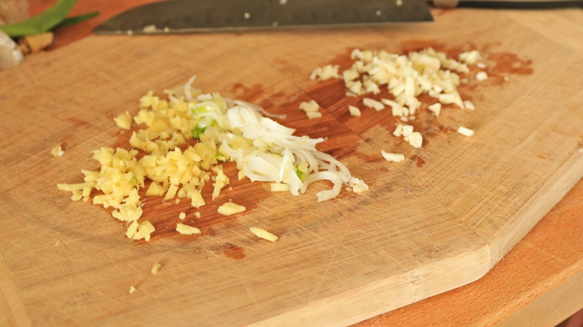 Minced ginger, garlic, and scallions on a cutting board.