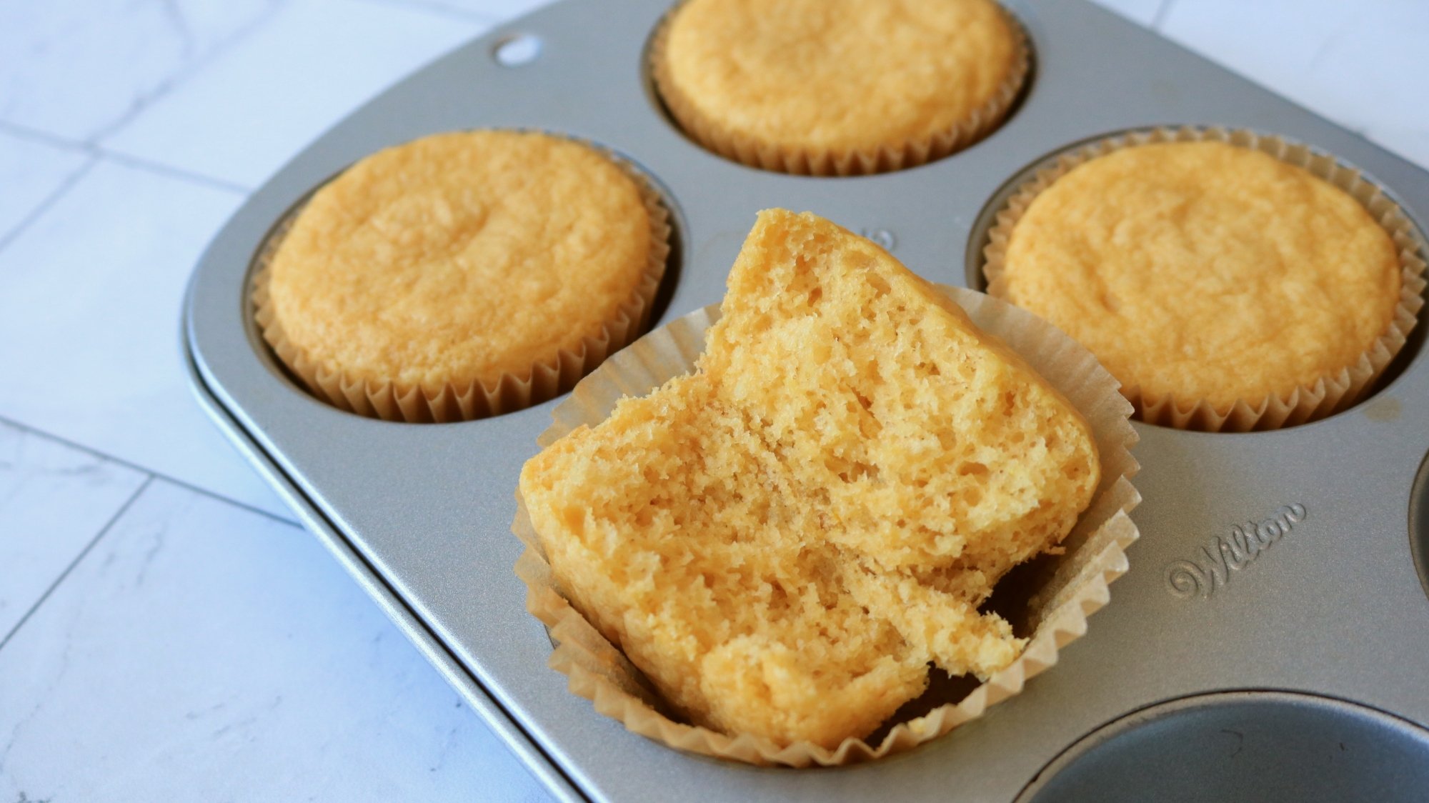 A cupcake broken in half and sitting on a cupcake pan.