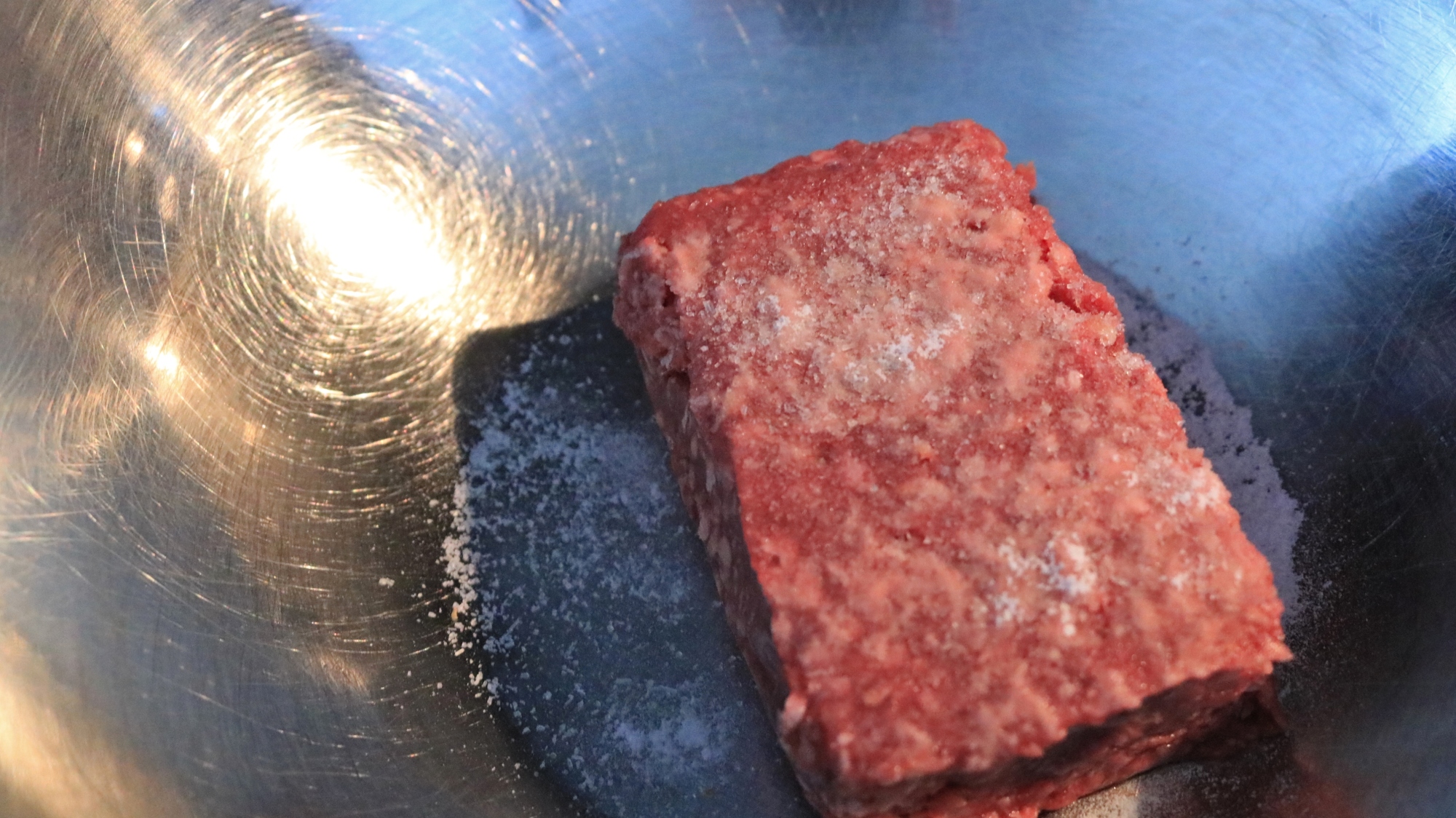 A rectangle of ground beef in a bowl with seasonings.