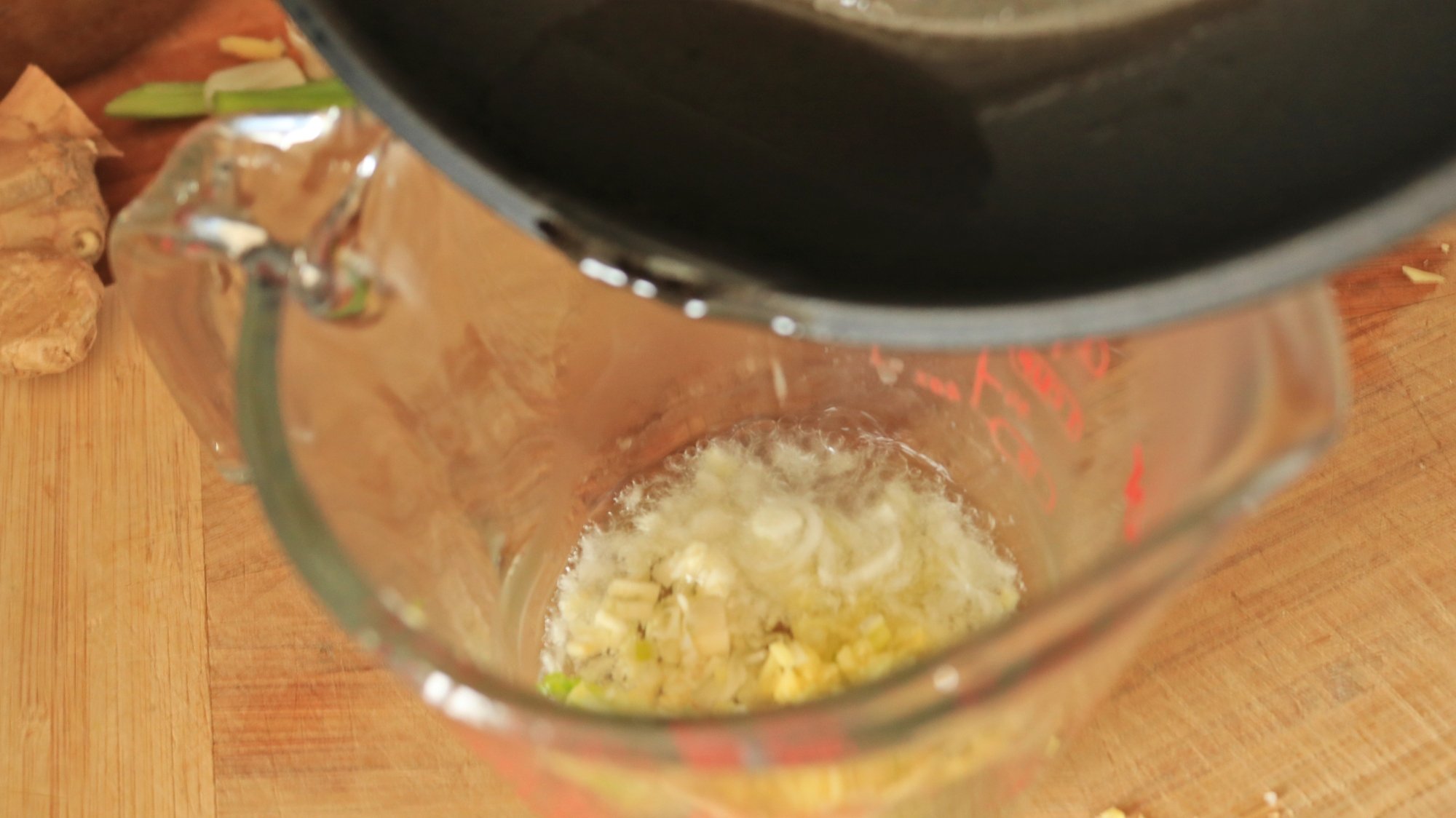 Oil pouring into a measuring cup of chopped aromatic ingredients.