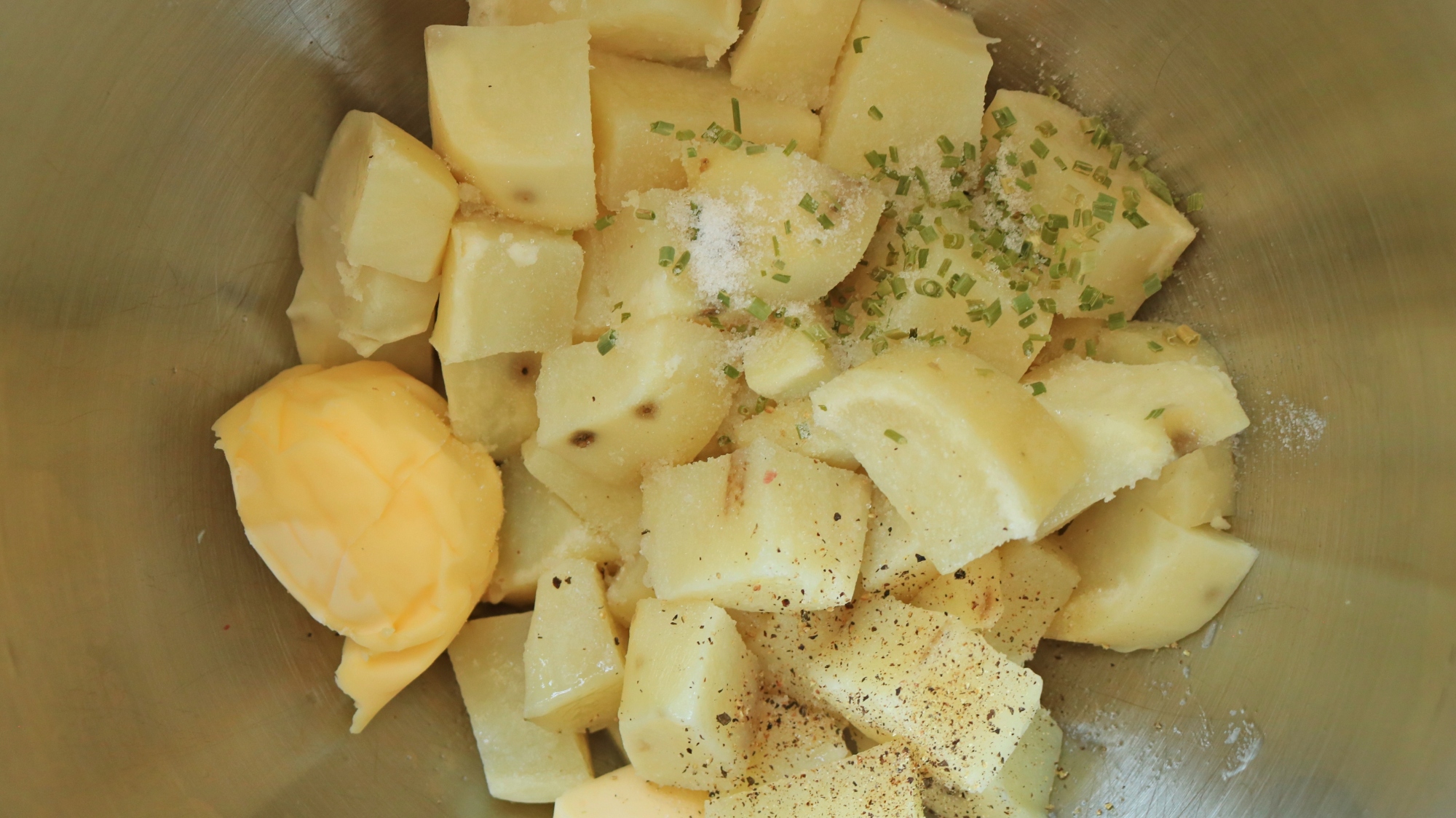 Cubed potatoes with butter and dry chives in a silver bowl.
