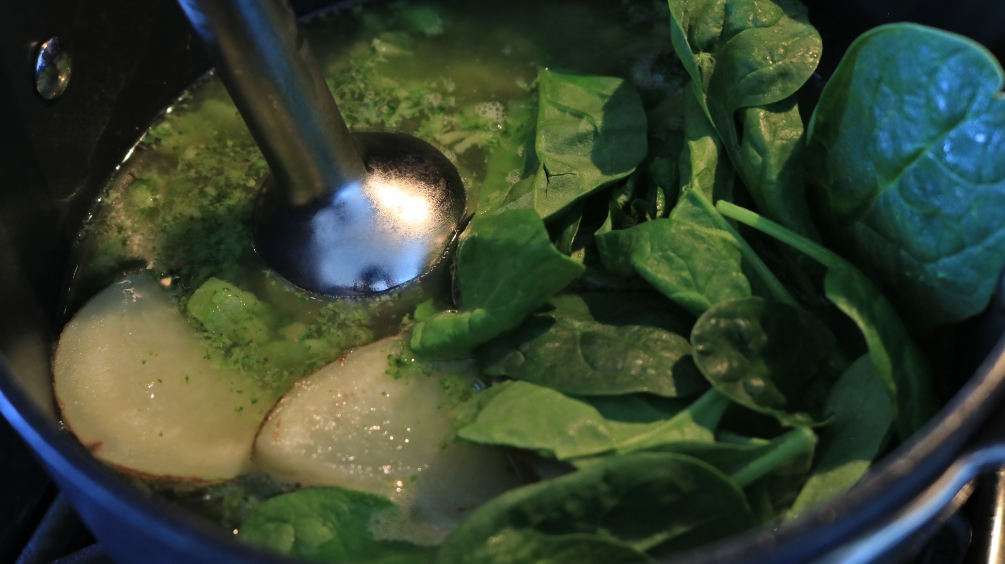 An immersion blender head in a pot of vegetables.