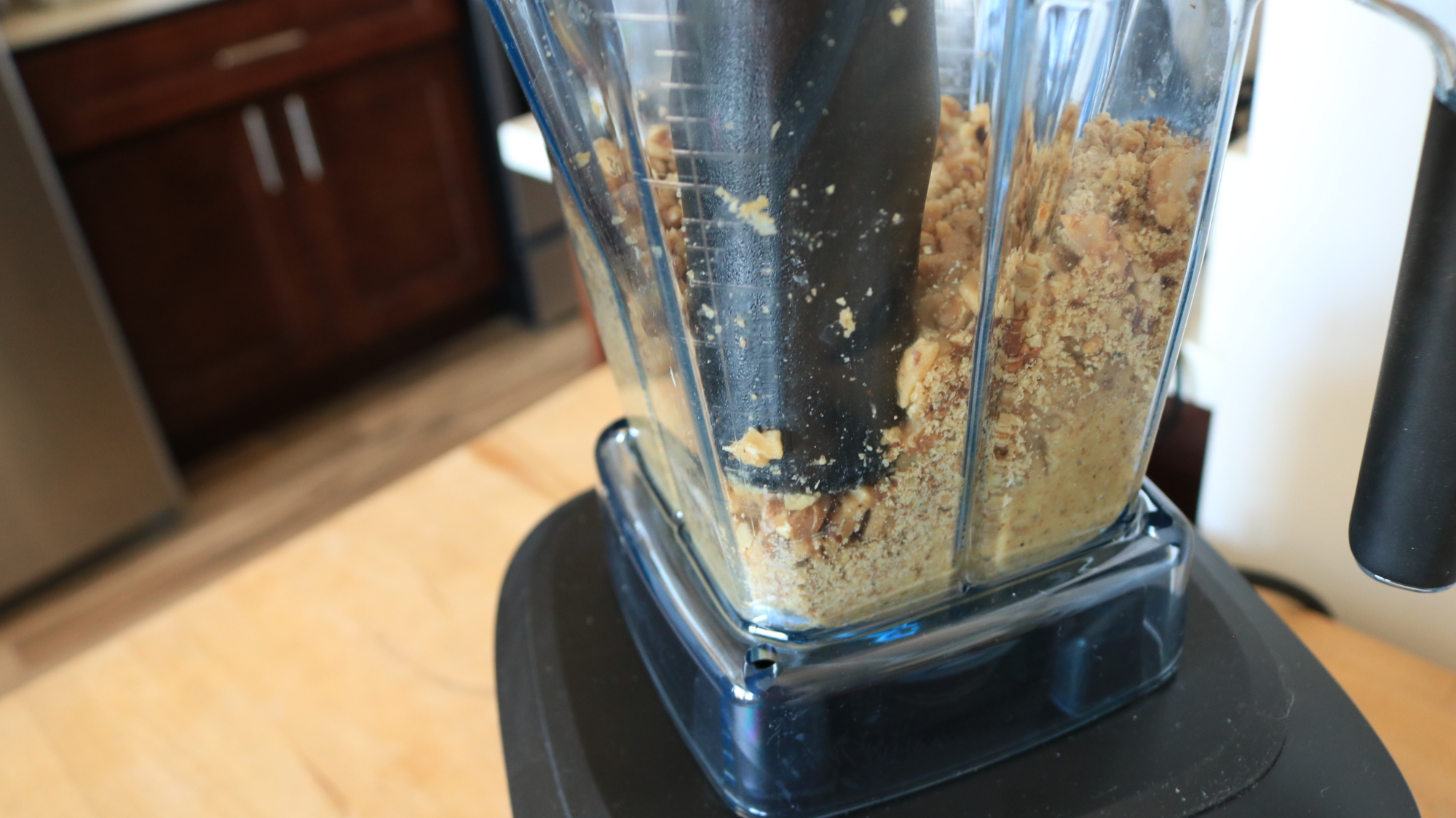 A plastic tamper pressing nut bits in a blender.