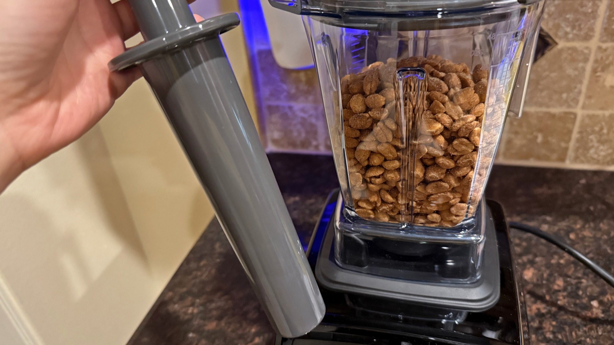 Vitamix blender tamper and peanuts in the blender behind it.