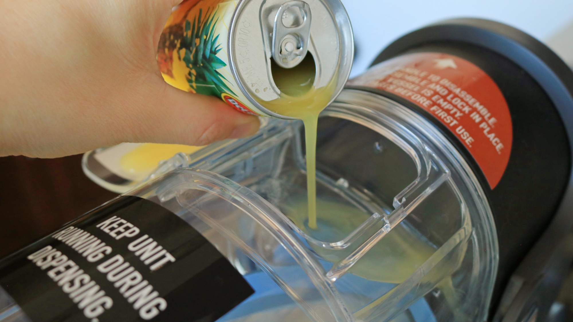 A hand pouring pineapple juice into the Ninja Slushi machine.