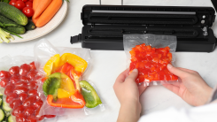 Hands seen sealing an airtight bad of produce using a vacuum sealer on a countertop, with plates of fresh produce nearby