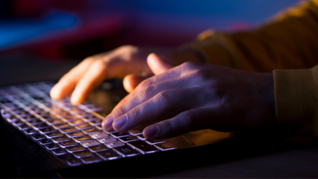 Man typing on a backlit keyboard in a dim room
